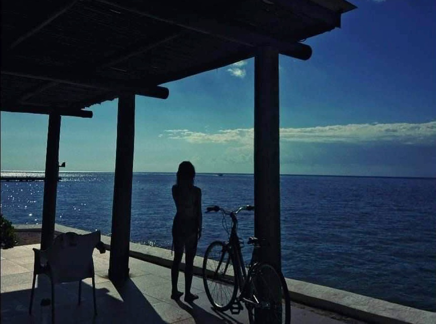 Mujer en la playa viendo al horizonte con una bicicleta